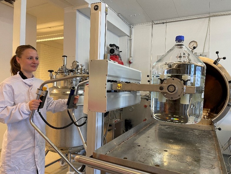 Una mujer que trabaja en la producción farmacéutica utiliza una carretilla elevadora TAWI para manipular botellas grandes.