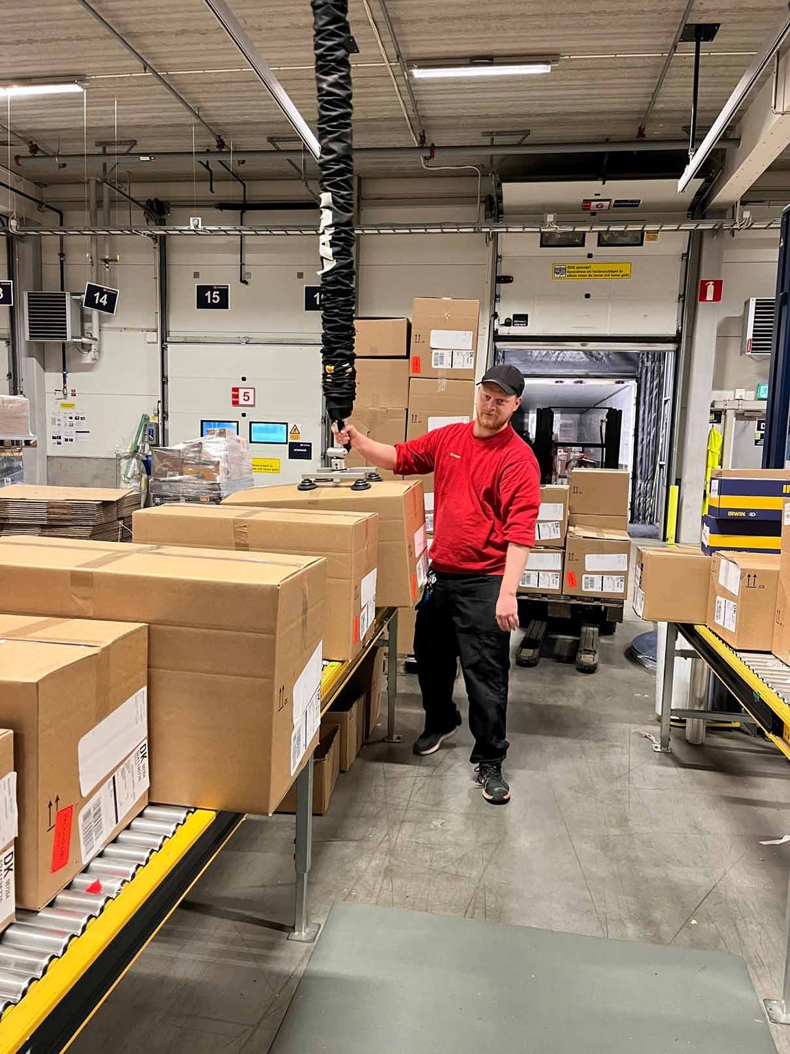Operaio che solleva casse presso DB Schenker con sollevatori a vuoto TAWI