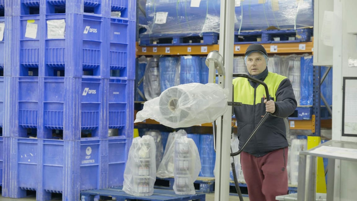 Hombre en una planta de producción alimentaria utilizando una carretilla elevadora TAWI para transportar bobinas de embalaje.