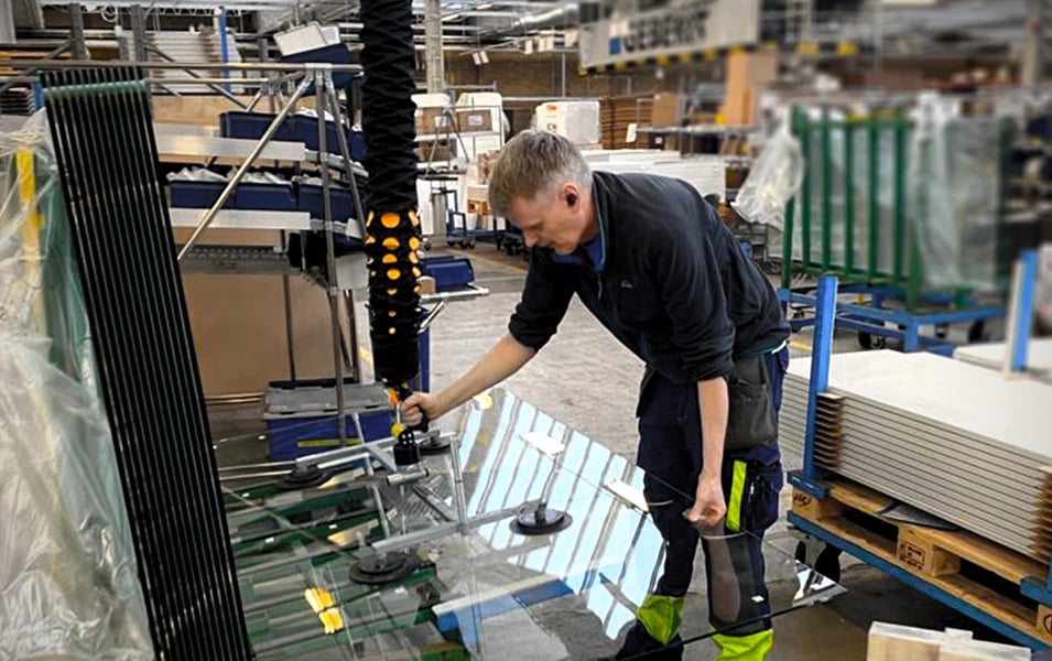 Man i fabrik lyfter glasskiva med vakuumlyft