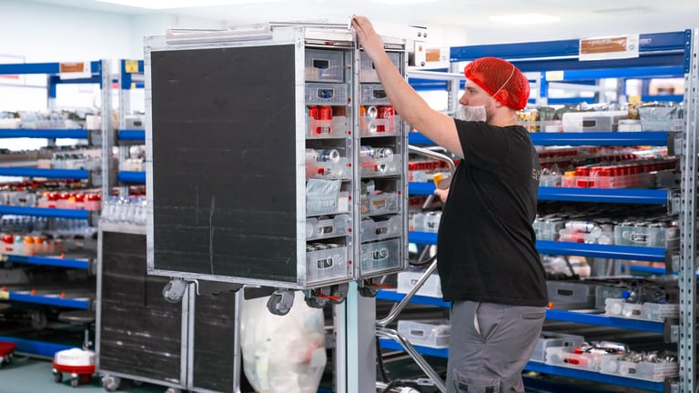A person uses a TAWI trolley to lift an airline trolley to a good height for loading items.