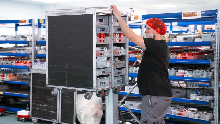 A person uses a TAWI trolley to lift an airline trolley to a good height for loading items.