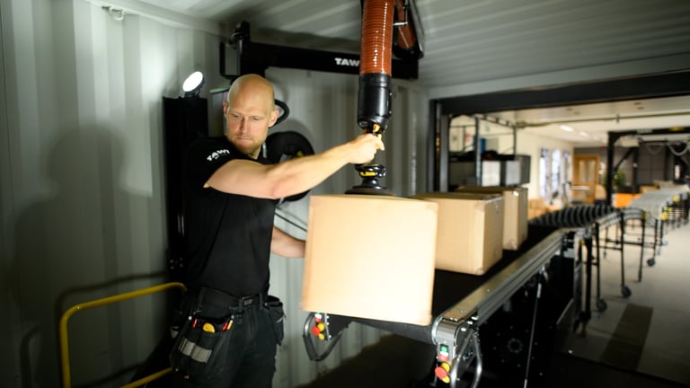 Une personne utilise le déchargeur de conteneurs TAWI pour manipuler des cartons