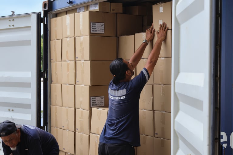 Workers try to unload a shipping container manually.