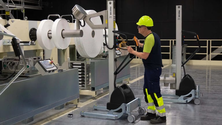 Man in packaging production mounting rolls with TAWI lifting trolley