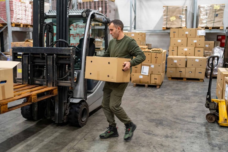 Operatore che porta a mano una scatola verso un muletto con pallet