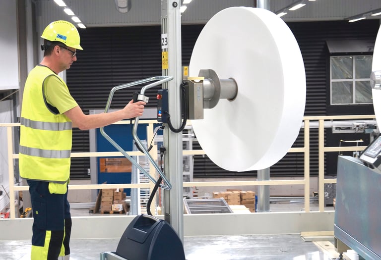 A worker lifts a large reel with a TAWI lifting trolley.