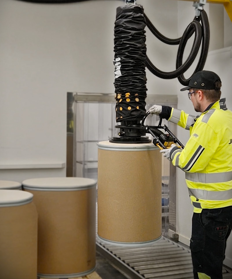 Man in production at Jacobi Resins lifting large drums with a TAWI vacuum lifter