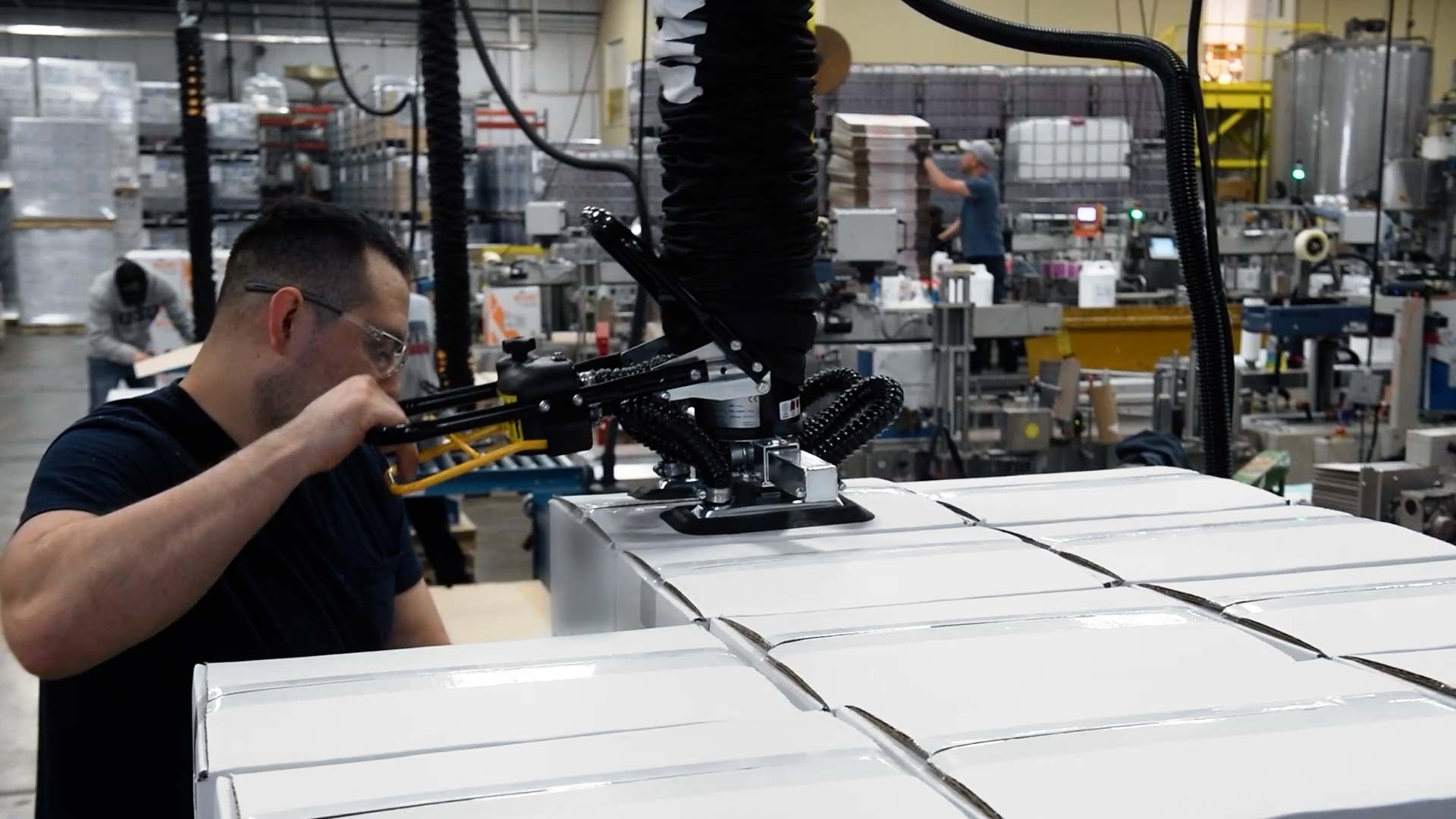 Workers at Exacto using TAWI vacuum lifters to palletize end of line packaging