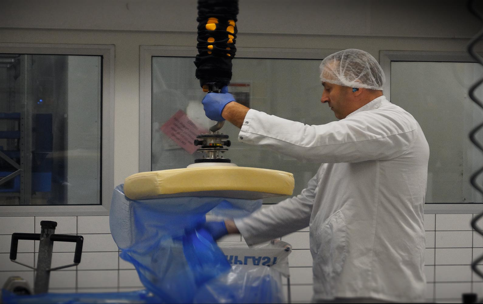 Male food production worker lifting large cheese blocks with TAWI vacuum lifter