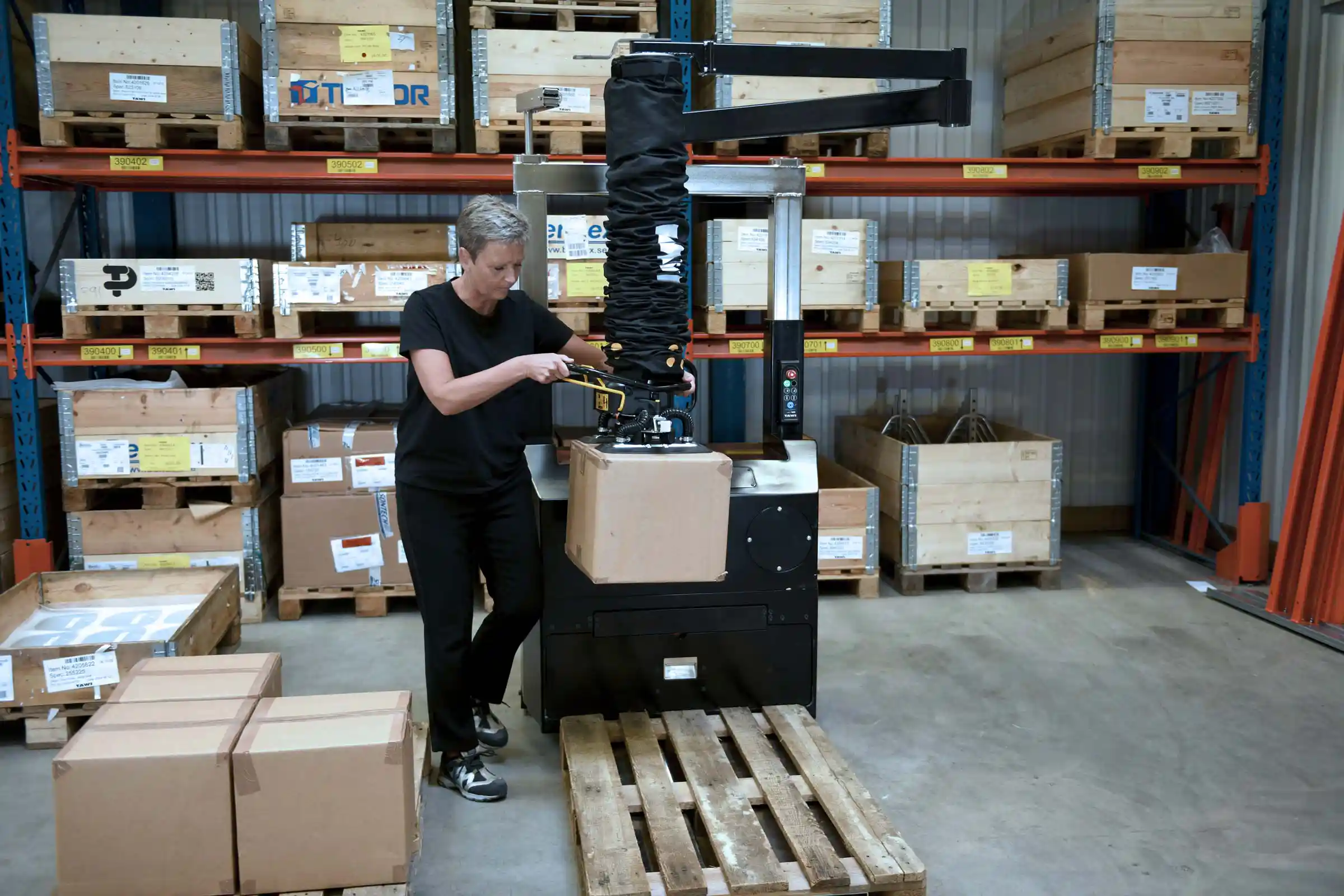 Woman in warehouse using smart lifting equipment from TAWI to lift and palletise boxes