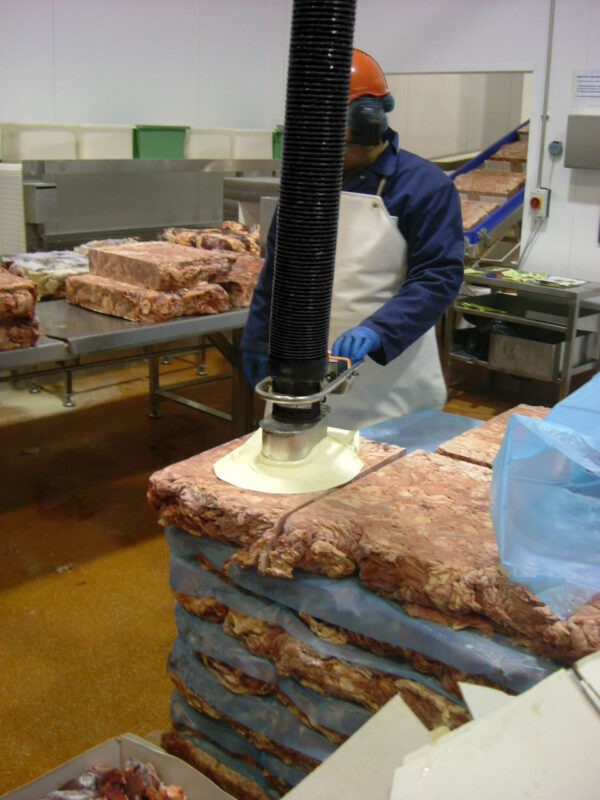 Man lyfter block av kött med en rostfri vakuumlyft i fabrik