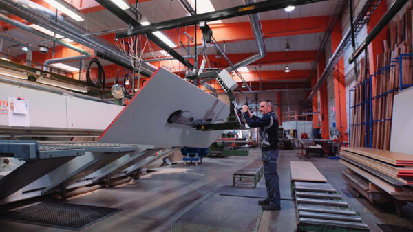 Man lifting large sheet of wood into CNC machine using vacuum gripper