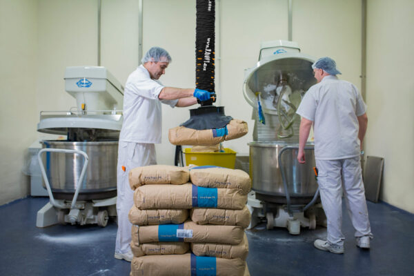 Two men lifting paper sack with food using handhold vacuum lifter