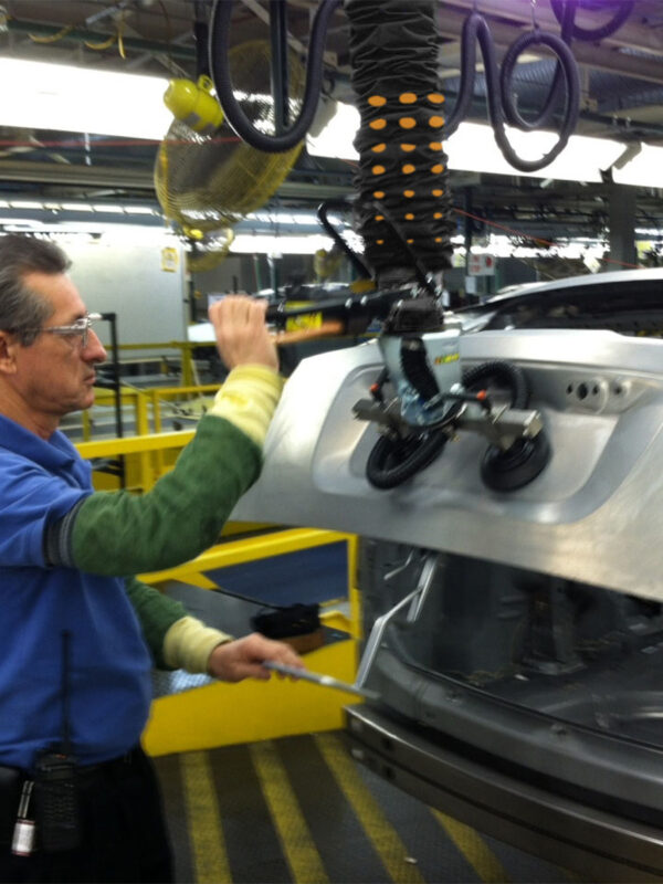 Personal i bilfabrik lyfter bagagelucka med hjälp av en skräddarsydd vakuumlyft
