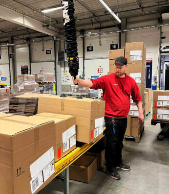 Medarbejder på DB Schenker løfter kasser med vakuumløft