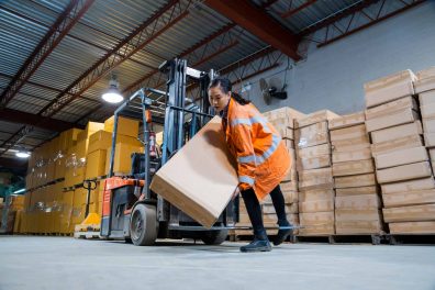 Female worker carrying a large package and sitting on a forklift