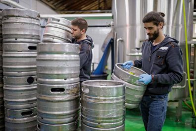 Two male workers in a brewery lifting kegs