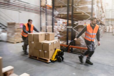 Two men pulling a fork lift with palletized boxes in a warehouse
