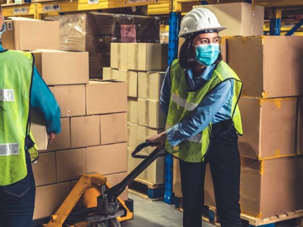 Two women with a fork lift picking boxes in a warehouse and placing on pallet