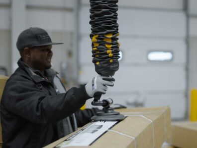 Mannlig lagerarbeider som bruker en TAWI vakuumløfter til å palletere esker